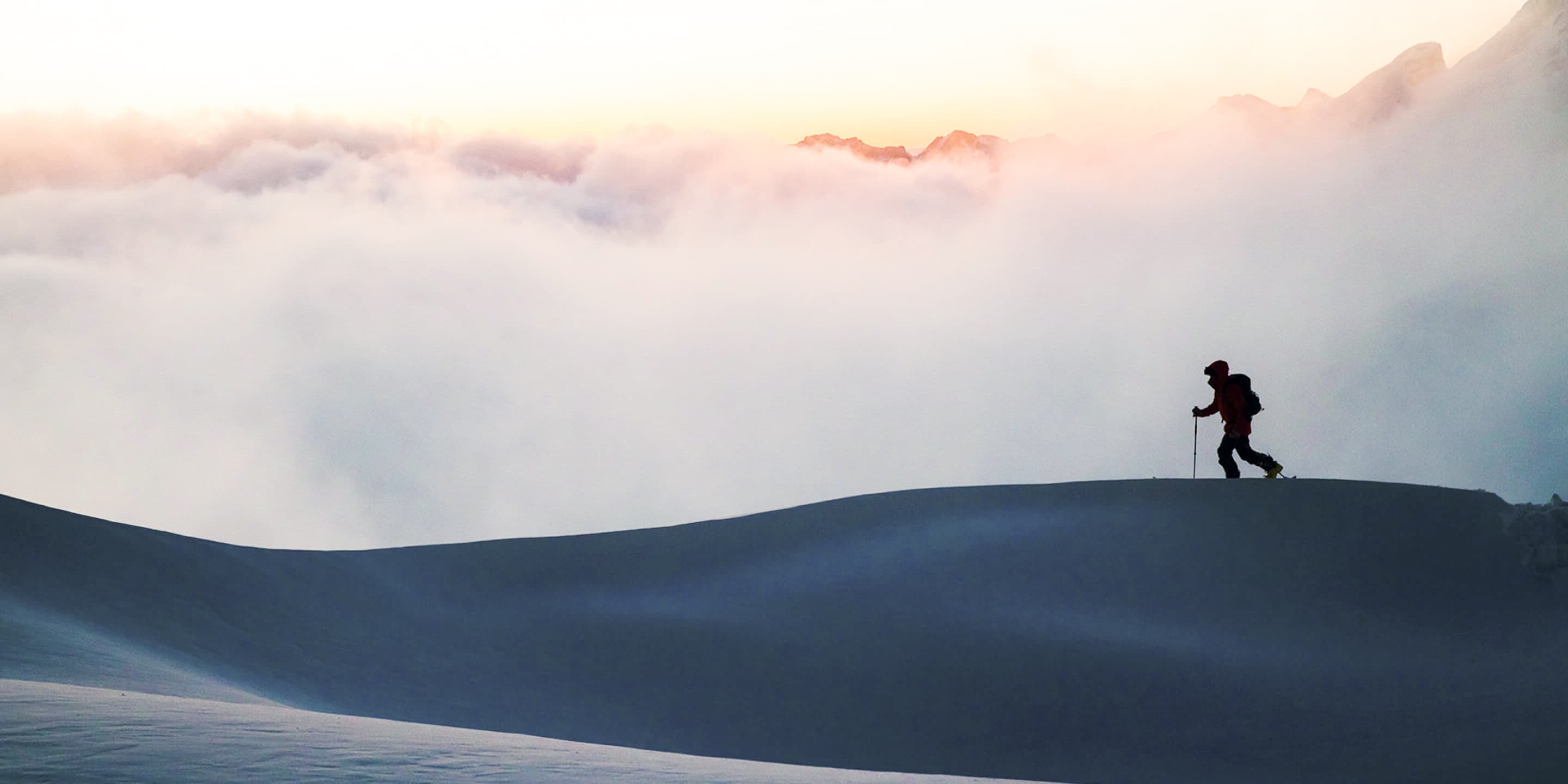 A guy ski touring with sunset in the background