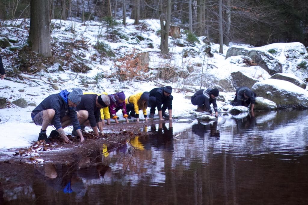 Group of friends putting their hands under icy waters in Poland.