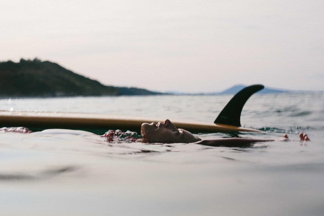 Longboard Girl resting in the Ocean with the fin of her board sticking out of the water.