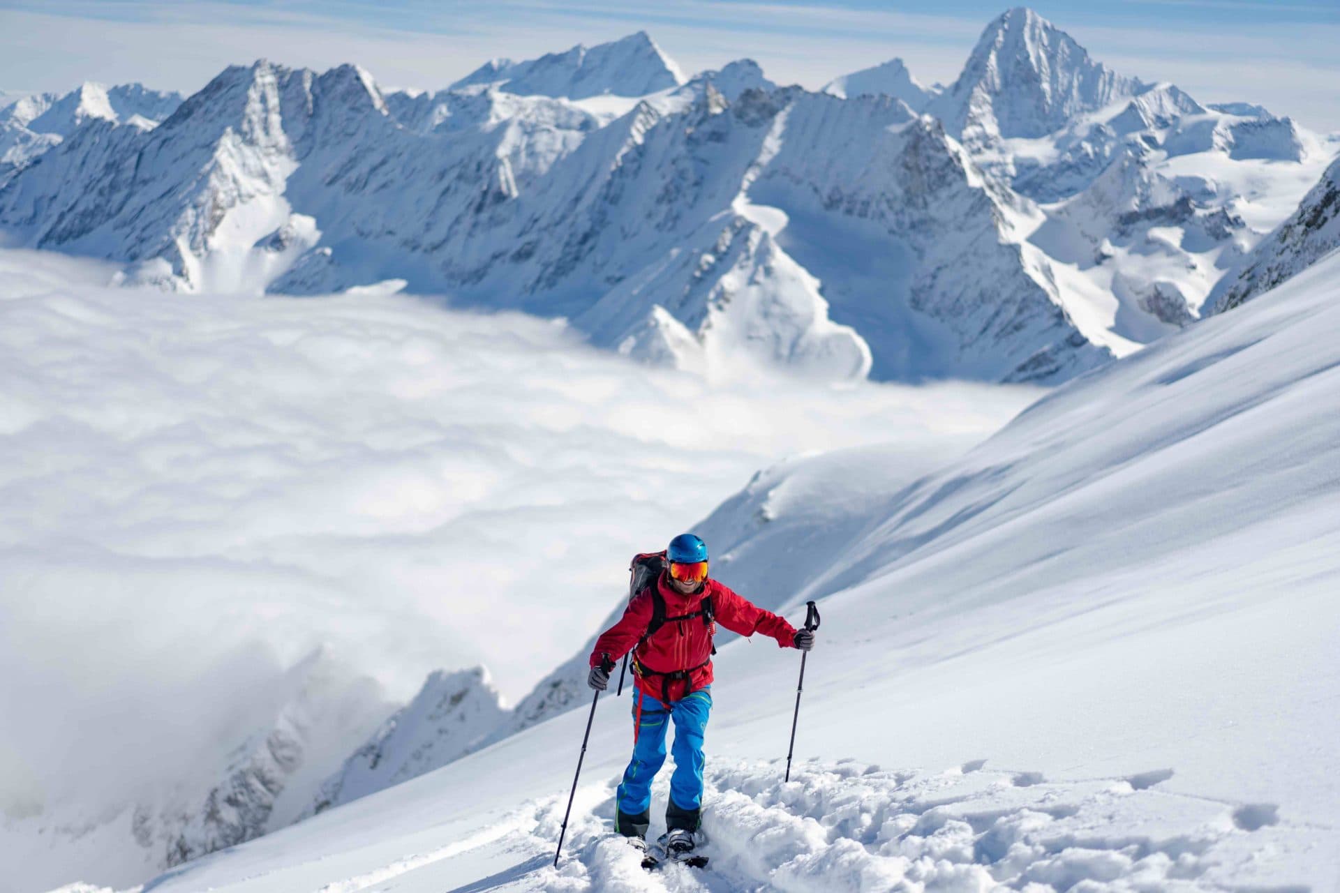 Ski tourer having the view of the alps and the clouds below him
